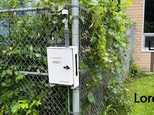 A white box on a pole next to a fence  Description automatically generated